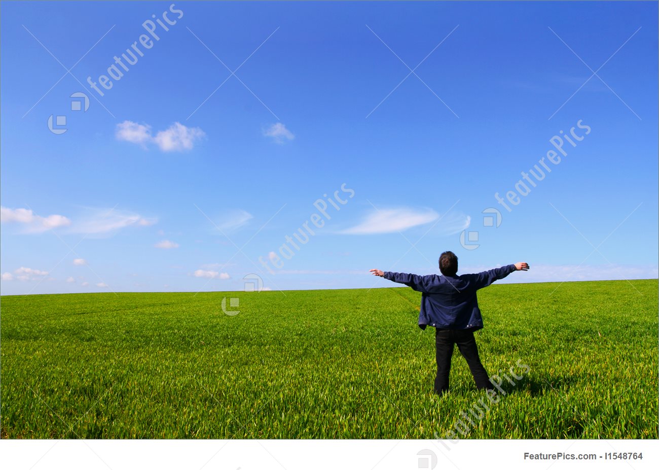 A man alone in a green field, breathing the air with open arms
