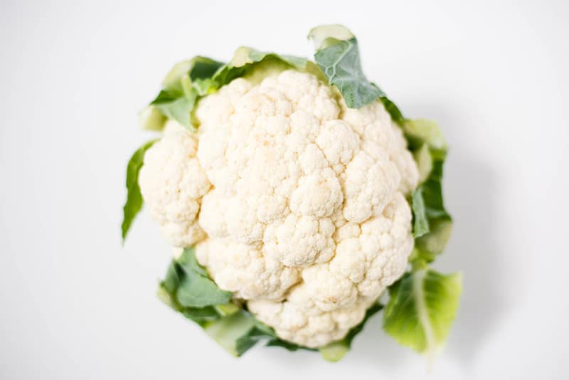 A single fresh cauliflower which still has the leaves attached and can be  cut up and