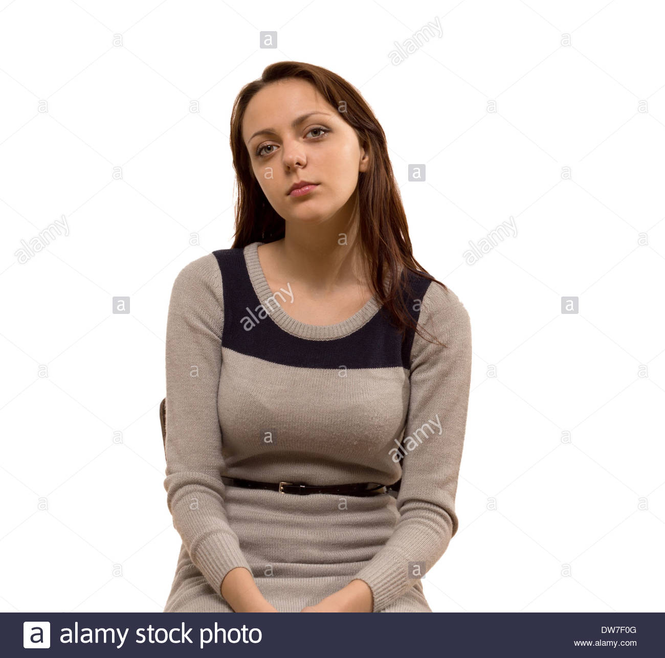 Busty atractiva mujer joven con cabello marrón largo demurely sentado con  sus manos en su regazo, mirando a la cámara con una expresión seria,