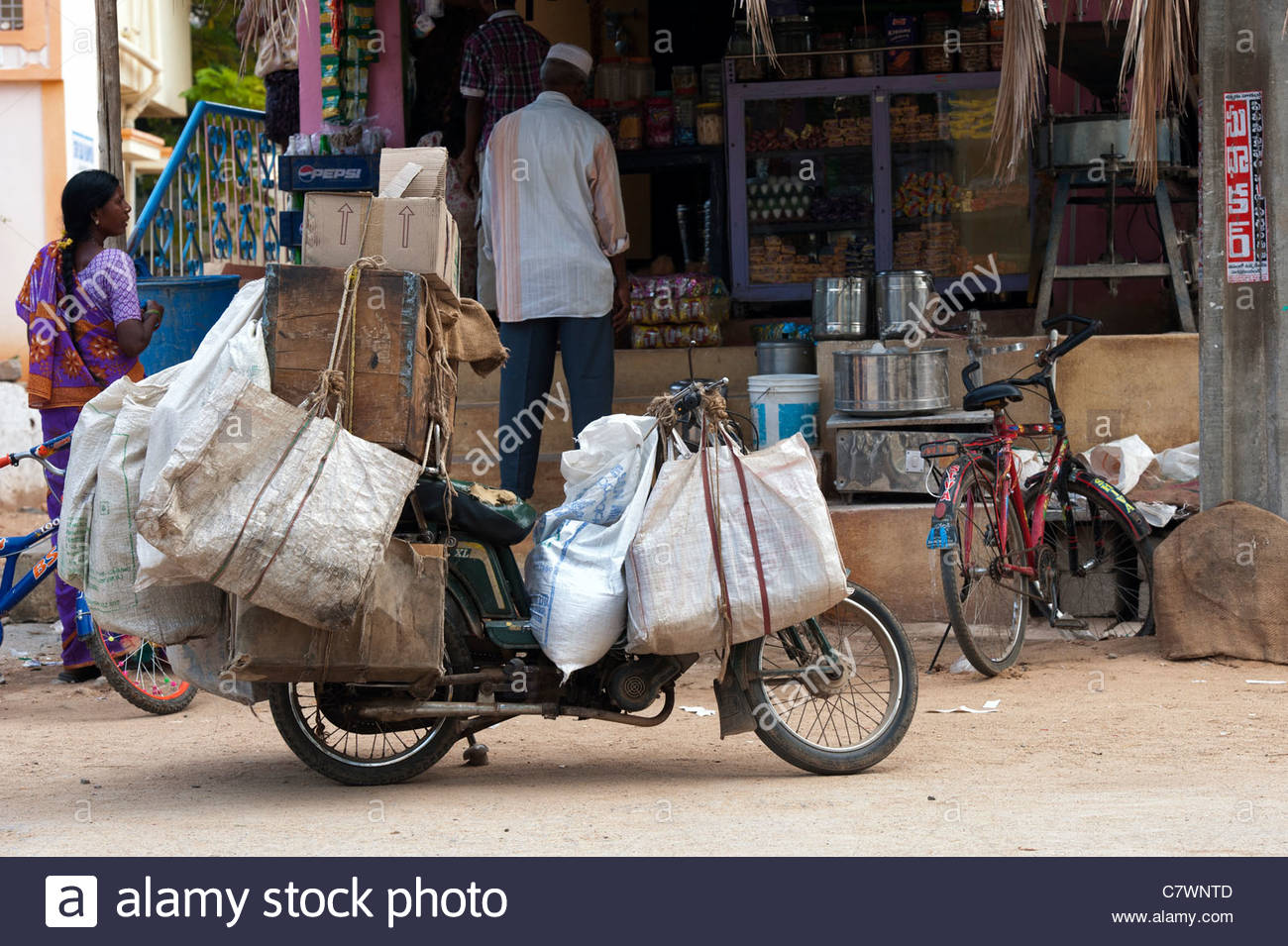 Ciclomotor ladened indio con mercancías para vender a las tiendas locales  en las calles de Puttaparthi